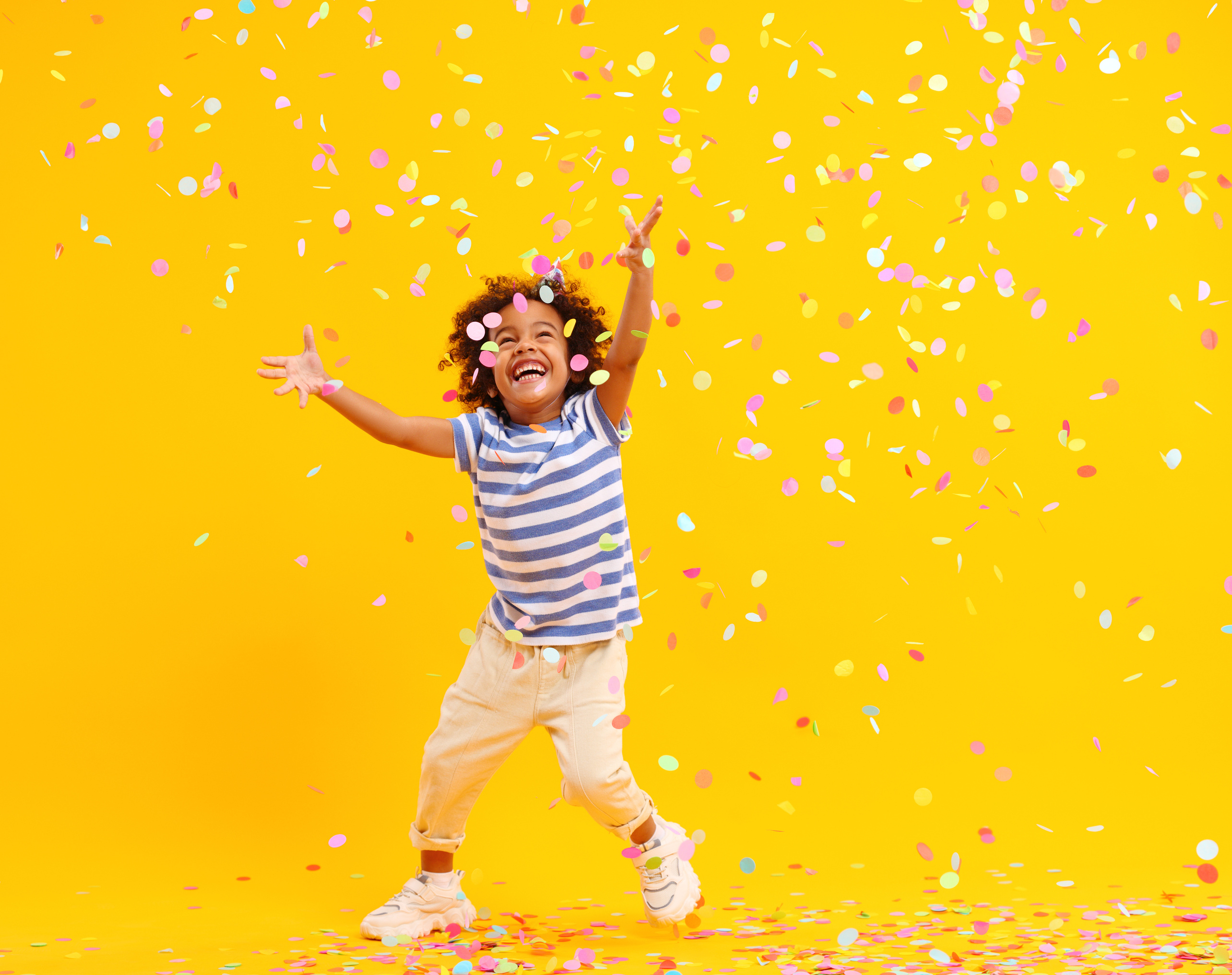 Excited African American kid jumping and catching confetti in studio